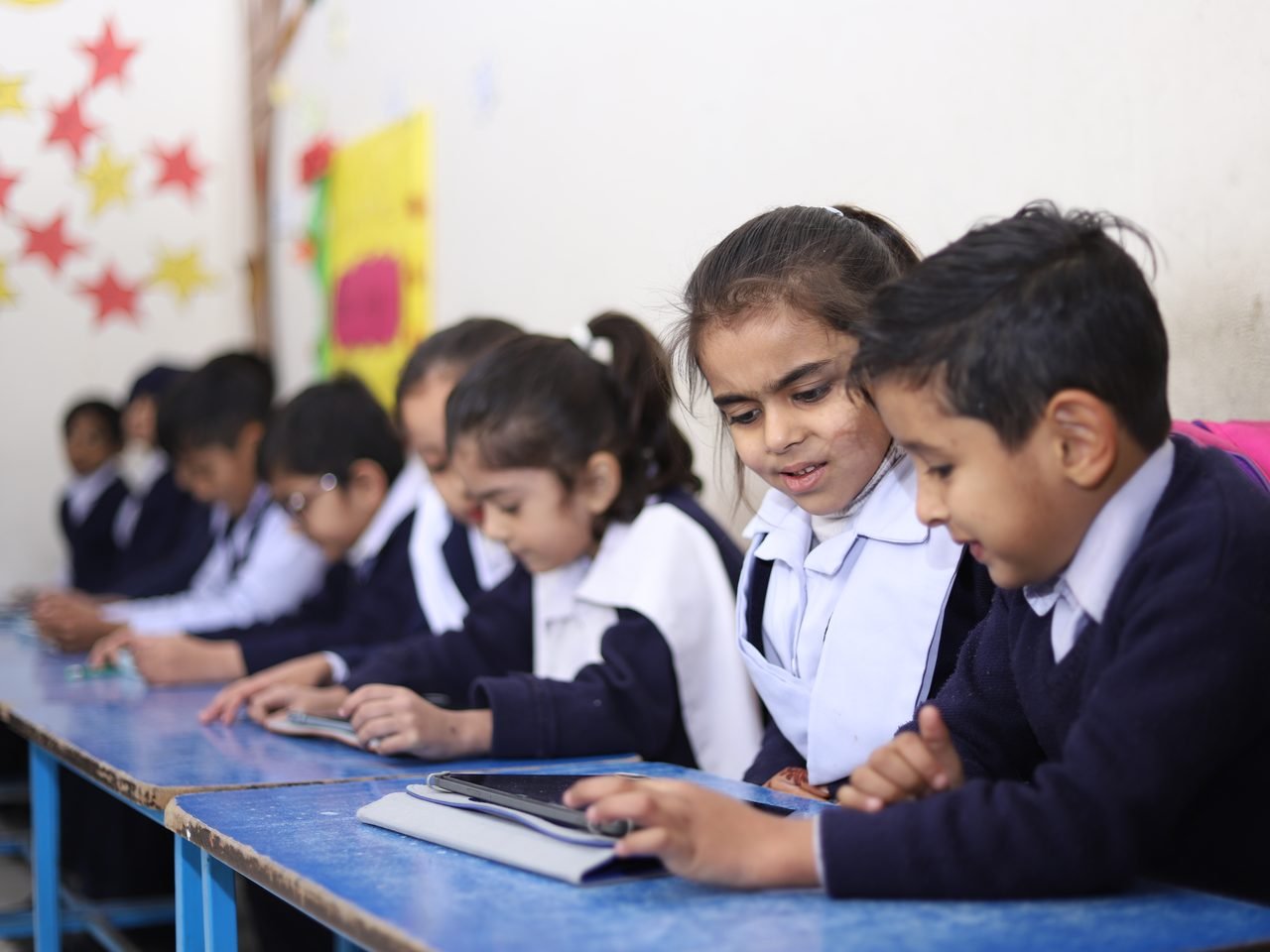 A row of kindergarten children tapping through a lesson on tablets in class