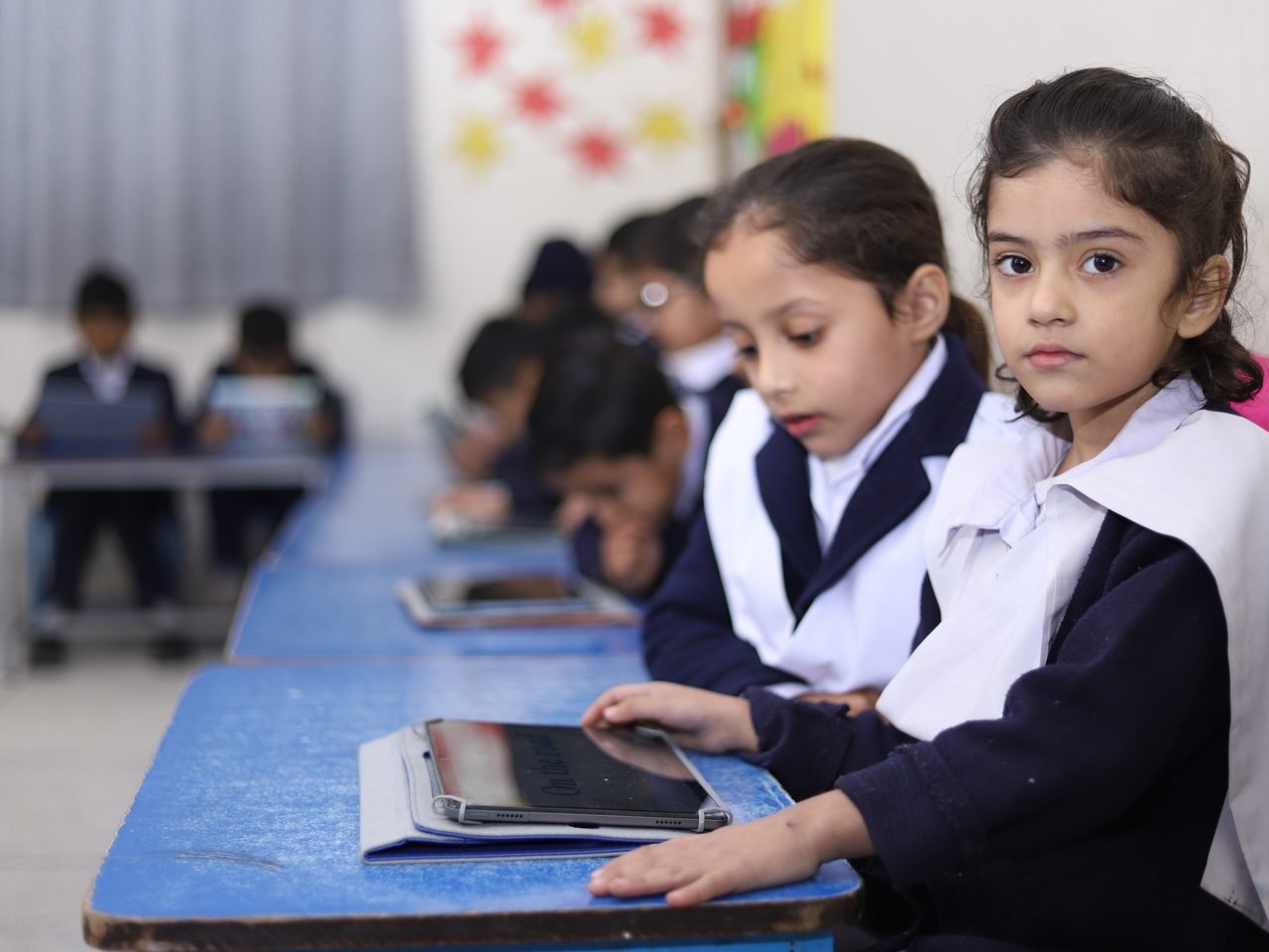 Kindergarten pupils in uniform working on tablets at their classroom desks